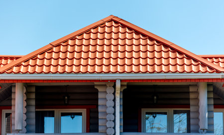 A red roof with a gutter on the side of a building. The roof is slanted and has a triangular shapeの写真素材