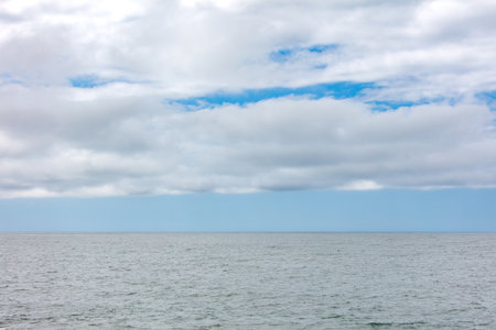 The sky is cloudy and the ocean is calm. The clouds are white and the sky is blueの写真素材