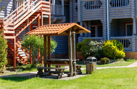 A wooden picnic table with a roof is in a grassy area. The table is surrounded by trees and bushesの写真素材