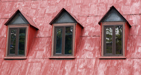 Three windows on a red roof with a brown frame. The windows are all facing the same directionの写真素材