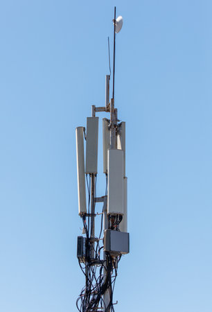 A tall tower with many antennas on top. The sky is clear and blue. The tower is a cell phone tower