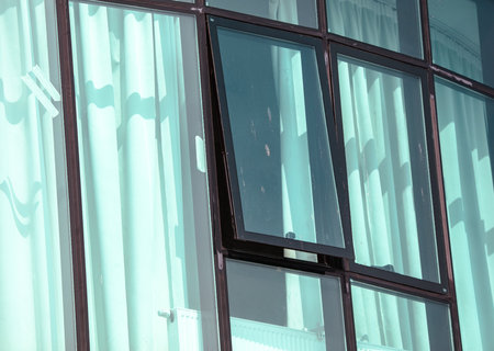 A window with a black window pane and a white curtain. The curtain is open and the window is closedの写真素材