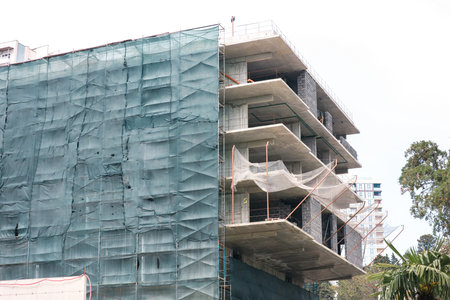 A building under construction with scaffolding and a tarp covering the top. The building is tall and has a modern designの写真素材