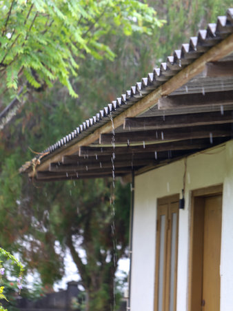 A house with a roof that is leaking. The rain is falling on the roof and the groundの写真素材