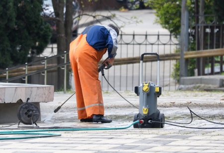 A man in orange jumpsuit is cleaning a sidewalk with a pressure washer. The scene is calm and peaceful, with the man focused on his taskの写真素材