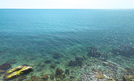 The ocean is calm and clear, with a few rocks scattered along the shore. The water is a deep blue color, and the sky is a bright blue color. The scene is peaceful and sereneの写真素材