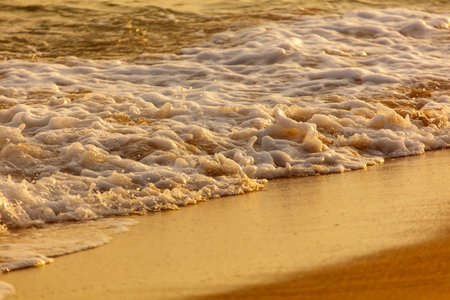 The ocean waves are crashing onto the shore, creating a beautiful and calming scene. The water is a mix of white foam and brown sand, giving it a unique and serene appearanceの写真素材