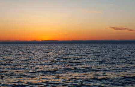 The ocean is calm and the sky is a beautiful orange color. The sun is setting and the water is reflecting the colors of the skyの写真素材