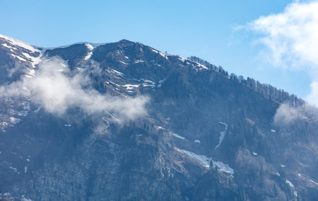 A mountain covered in snow with a cloudy sky in the background. The clouds are white and fluffy, giving the scene a peaceful and serene atmosphereの写真素材