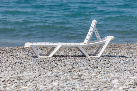 A white beach chair is laying on the beach. The chair is empty and the beach is calmの写真素材
