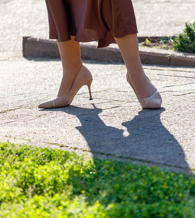 A woman wearing a brown dress and high heels is walking on a sidewalk. Concept of elegance and sophistication, as the woman's atmosphereの写真素材