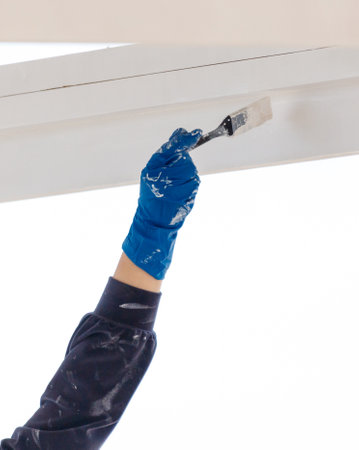 A person is painting a wall with a brush. The person is wearing blue gloves. The wall is whiteの写真素材
