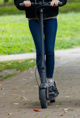 A woman is riding a scooter down a sidewalk. Concept of freedom and independence, as the woman is able to travel on her own without the need for a car or public transportationの写真素材