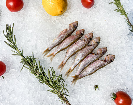 A close up of a fish display with a bunch of herbs and a lemon. The fish are arranged in a row and...