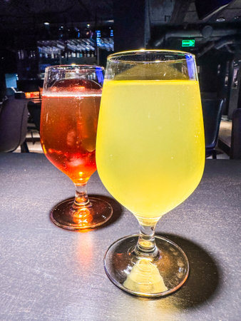 Two glasses of different colored drinks on a table. One is red and the other is yellowの写真素材