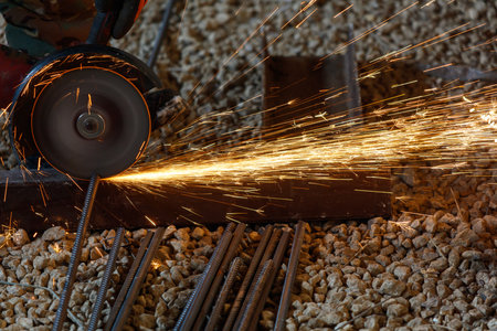 A man is cutting metal with a saw. The sparks from the saw are flying everywhere. Concept of danger and excitement, as the man is working with a potentially dangerous toolの写真素材
