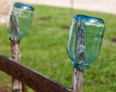 Two green vases are on a wooden fence post. The vases are empty and have a clear glass top. The fence post is made of wood and is located in a grassy areaの写真素材