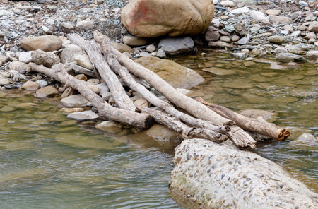 A river with a bridge made of logs. The logs are stacked on top of each other and are floating in the waterの写真素材