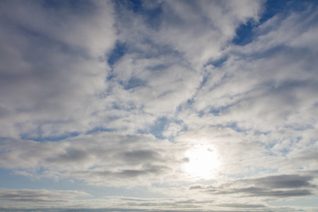 The sky is cloudy and the sun is shining through the clouds. The sun is bright and the sky is blueの写真素材