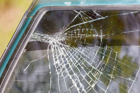 A car window is shattered with a spider web pattern. The spider web is made of broken glass and is scattered across the windshield. The scene is eerie and unsettlingの写真素材