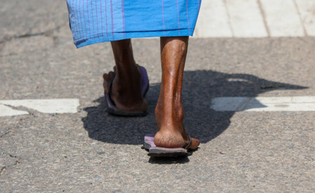 A man wearing flip flops walks down the street. The flip flops are purple and black