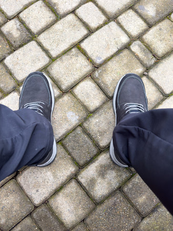 A person is standing on a brick sidewalk with their feet apart. The shoes are black and the pants are blackの写真素材