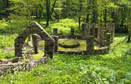 A stone building with a small archway in the middle of a lush green field. The building appears to be abandoned and the archway is openの写真素材