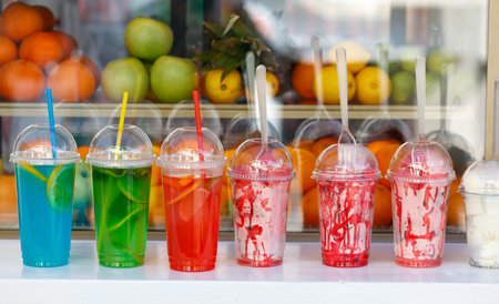 A row of colorful drinks with straws in them. The drinks are in plastic cups and are arranged in a...