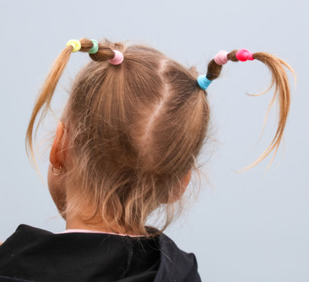 A young girl with her hair in pigtails. The pigtails are colorful and have a lot of beadsの写真素材