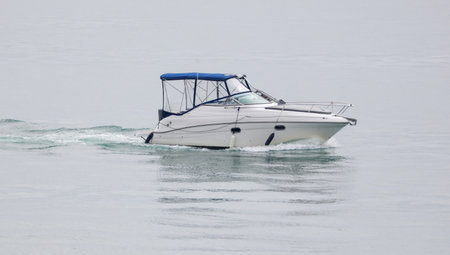 A small white boat is on the water. The boat is moving and the water is calm. The sky is cloudy and the water is clearの写真素材