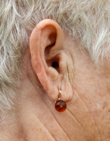 A woman with a gold earring with a brown stone in it. The earring is dangling from her earの写真素材