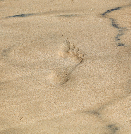 A foot print is in the sand. The sand is light brown and the foot print is dark brownの写真素材