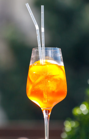 A glass of orange drink with straws in it is sitting on a table. The drink is in a wine glass, and the straws are in the glass as well. The drink appears to be a cocktailの写真素材