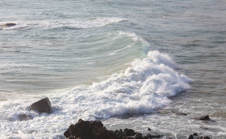 The ocean is calm and the waves are small. The water is a light blue color. The rocks are scattered...