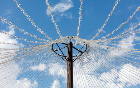 A tall pole with a heart-shaped structure on top. The structure is made of white strings and is suspended in the air. The sky above the pole is clear and blue, with a few clouds scattered throughoutの写真素材