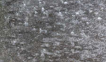 A wet sidewalk with raindrops falling on it. The rain is coming down in a steady stream, creating a gloomy and wet atmosphereの写真素材