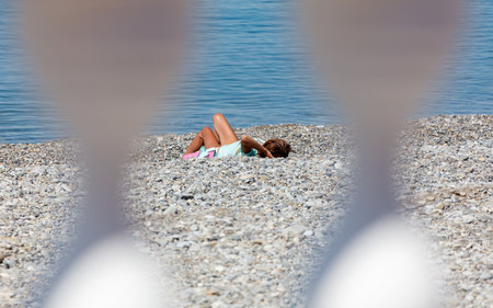 A girl is laying on the beach, looking at the water. The beach is rocky and the water is calmの写真素材