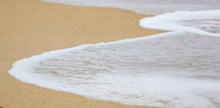 A beautiful beach with a large wave crashing onto the shore. The water is white and the sand is brown, creating a serene and peaceful atmosphereの写真素材