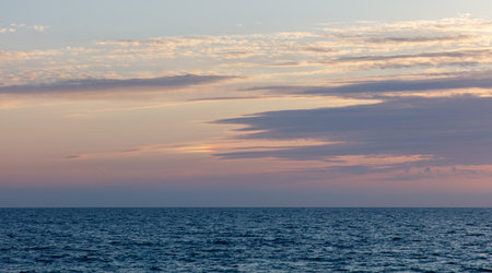 The sky is a beautiful shade of pink and blue. The ocean is calm and peaceful. The clouds are scattered throughout the sky, creating a sense of movement and depthの写真素材