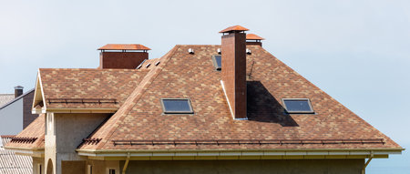 A house with a brown roof and a chimney. The roof is slanted and has a few windowsの写真素材