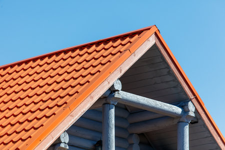 A red roof with a blue trim. The roof is slanted and has a wooden frame. The sky is clear and blueの写真素材