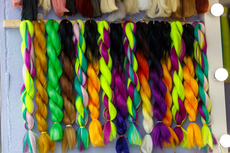 A row of colorful hair extensions are hanging on a wall. The colors include green, yellow, purple, and redの写真素材
