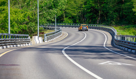 A car is driving down a road with a yellow line on the side. The road is empty and the car is the only vehicle on the roadの写真素材