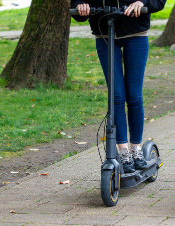 A woman is riding a scooter down a sidewalk. Concept of freedom and independence, as the woman is...