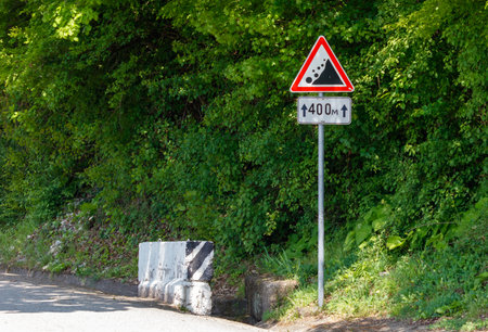 A sign with a red triangle and the number 400 on it is on a hillside. The sign is surrounded by trees and bushesの写真素材