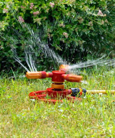 A red sprinkler is spraying water on a lawn. The water is coming out of the sprinkler in a circular patternの写真素材