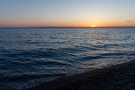 The ocean is calm and the sky is a beautiful orange color. The sun is setting in the distanceの写真素材