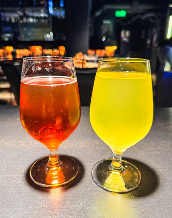 Two glasses of different colored drinks sit on a table. One is yellow and the other is redの写真素材