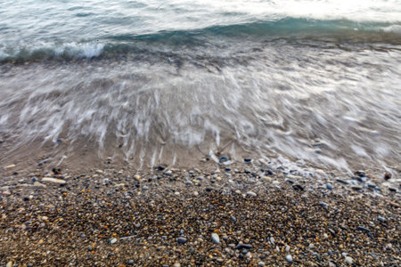 The ocean waves are crashing against the shore, creating a peaceful and calming atmosphere. The rocks on the beach add a sense of stability and grounding to the sceneの写真素材