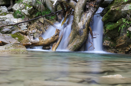 A stream of water flows down a rocky hillside. The water is clear and calm, and the rocks are scattered throughout the scene. Scene is peaceful and serene, as the water flows gently over the rocksの写真素材